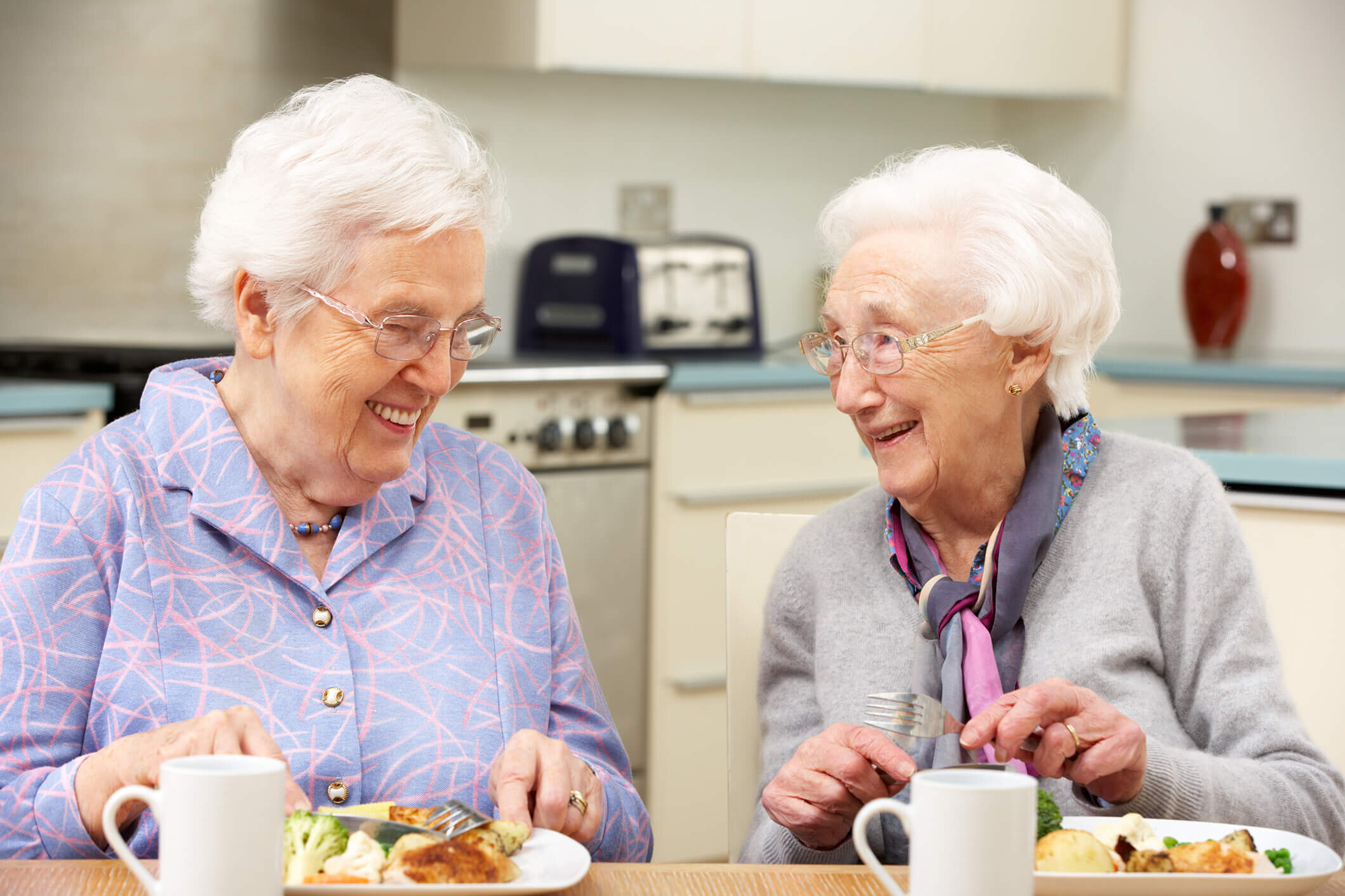Two residents sharing a meal and a laugh at the kitchen table